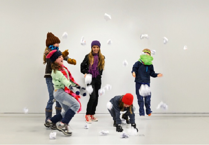 5 Kinder mit Mützen, Schals uns Handschuhen hüpfen und werfen Papierkugeln in die Luft
